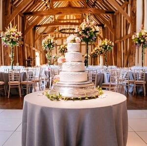 Micklefield Hall wedding, traditional white wedding cake in great barn with high flower centre pieces on tables behind