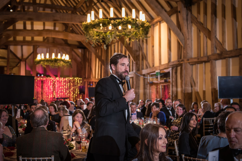 Man speaks to corporate gala dinner guests on microphone 
