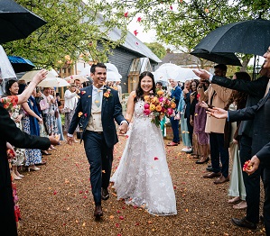Bride and groom having confetti thrown around them by their guests on their rainy wedding day at micklefield hall