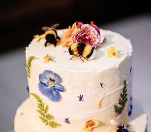 Beautiful cake made by the bride with white icing and vibrant florals. Topped with two bees
