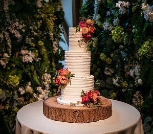 white wedding cake on a wooden log slice with orange, pink and green flowers